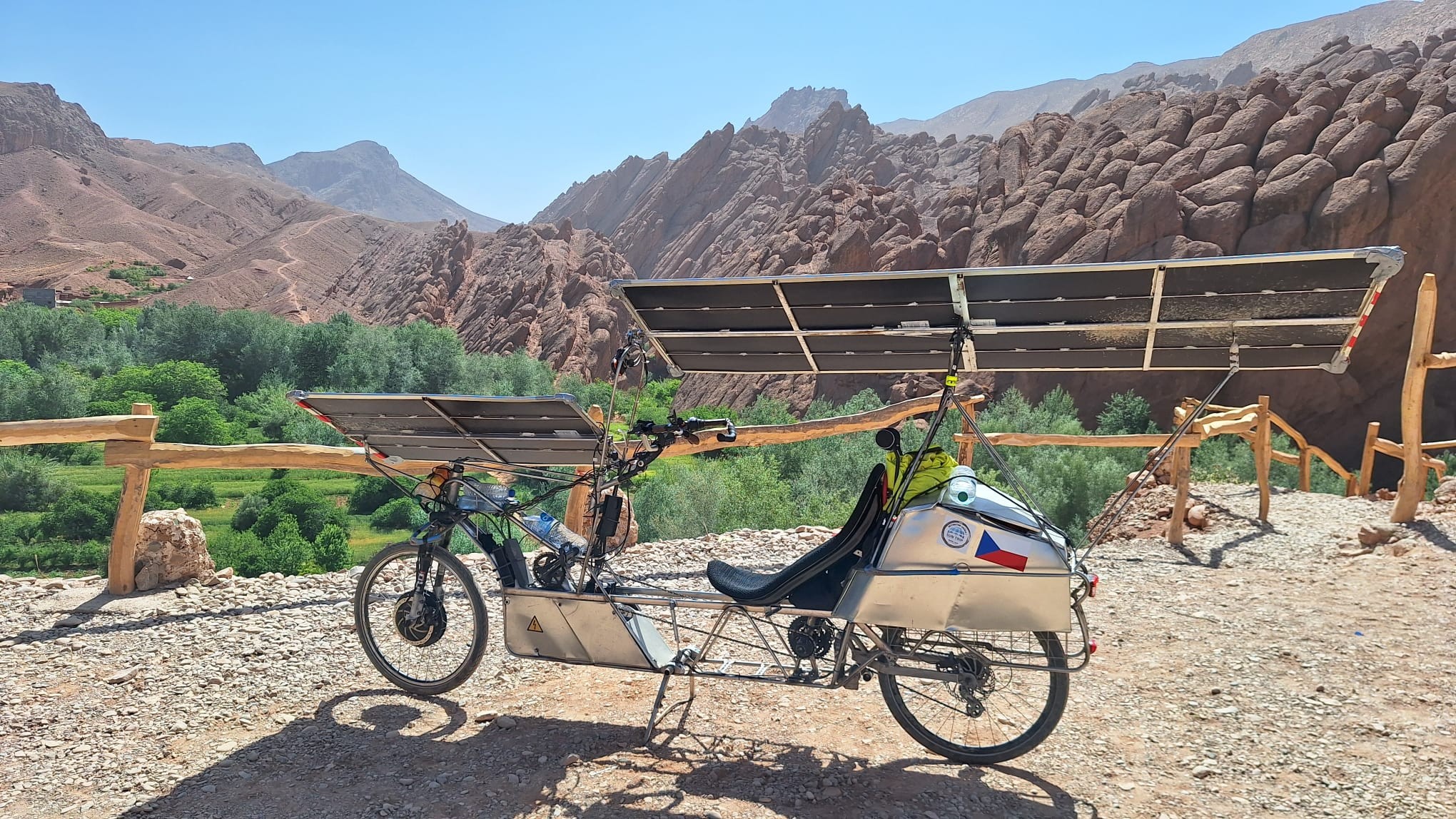 Solar bike parked at Dades gorge viewpoint. Green oasis on valley floor, brown scenic rocks, blue sky.