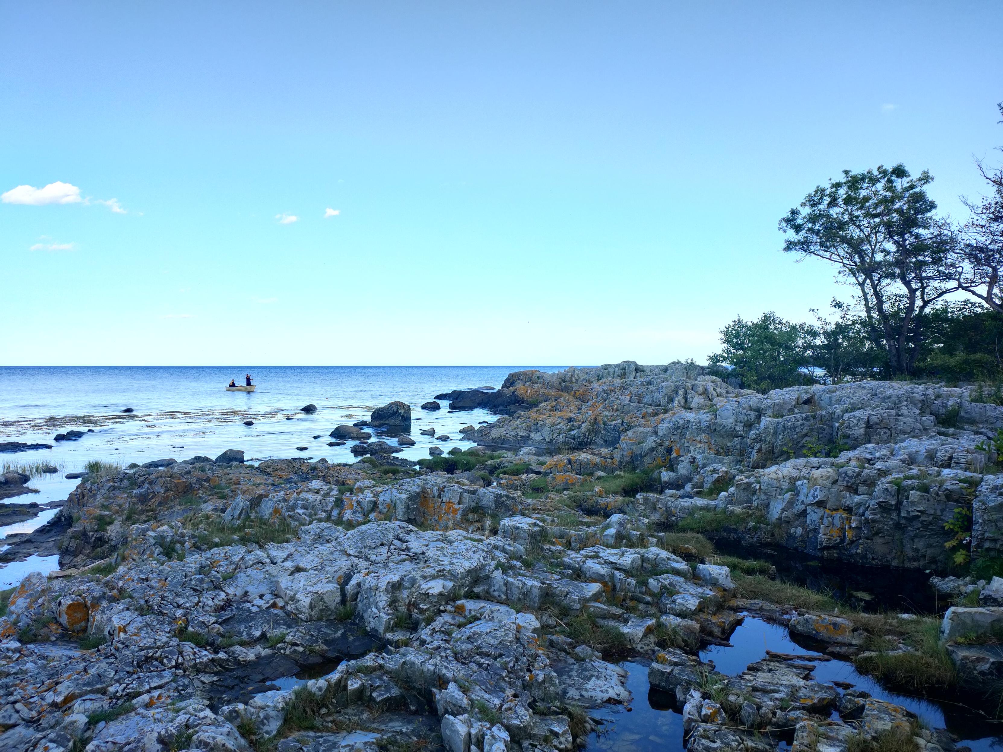 Photo of rocky coastline with small fishing boat and 2 people pulling the nets.